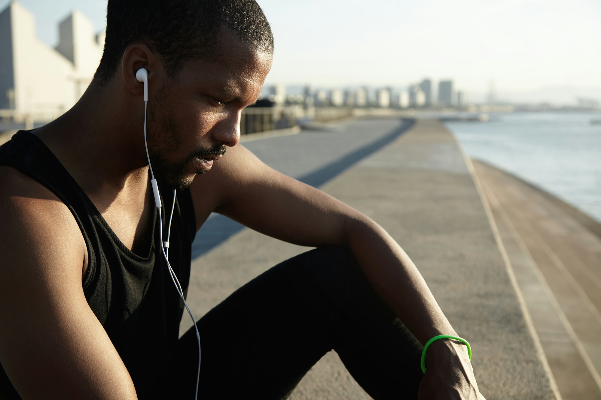 Good-looking muscular African athlete in sportswear sitting on top of stone stairs, looking down wit